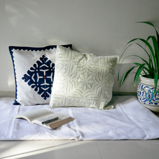 Handcrafted cushion cover with an orange and beige geometric pattern, placed on a couch next to a potted plant and a book.