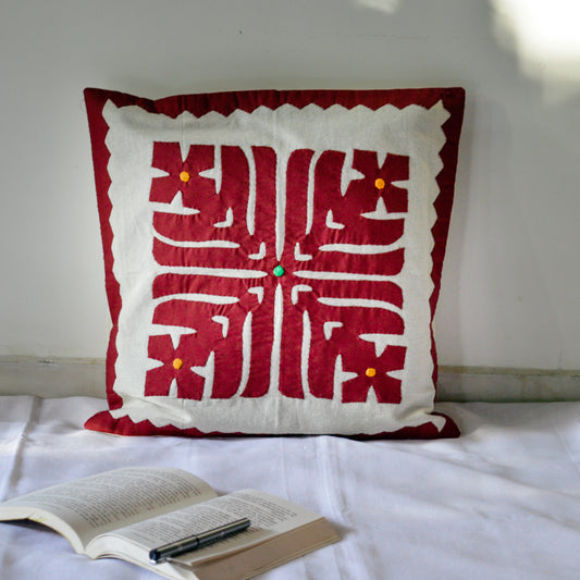 Handcrafted cushion cover with an orange and beige geometric pattern, placed on a couch next to a potted plant and a book.