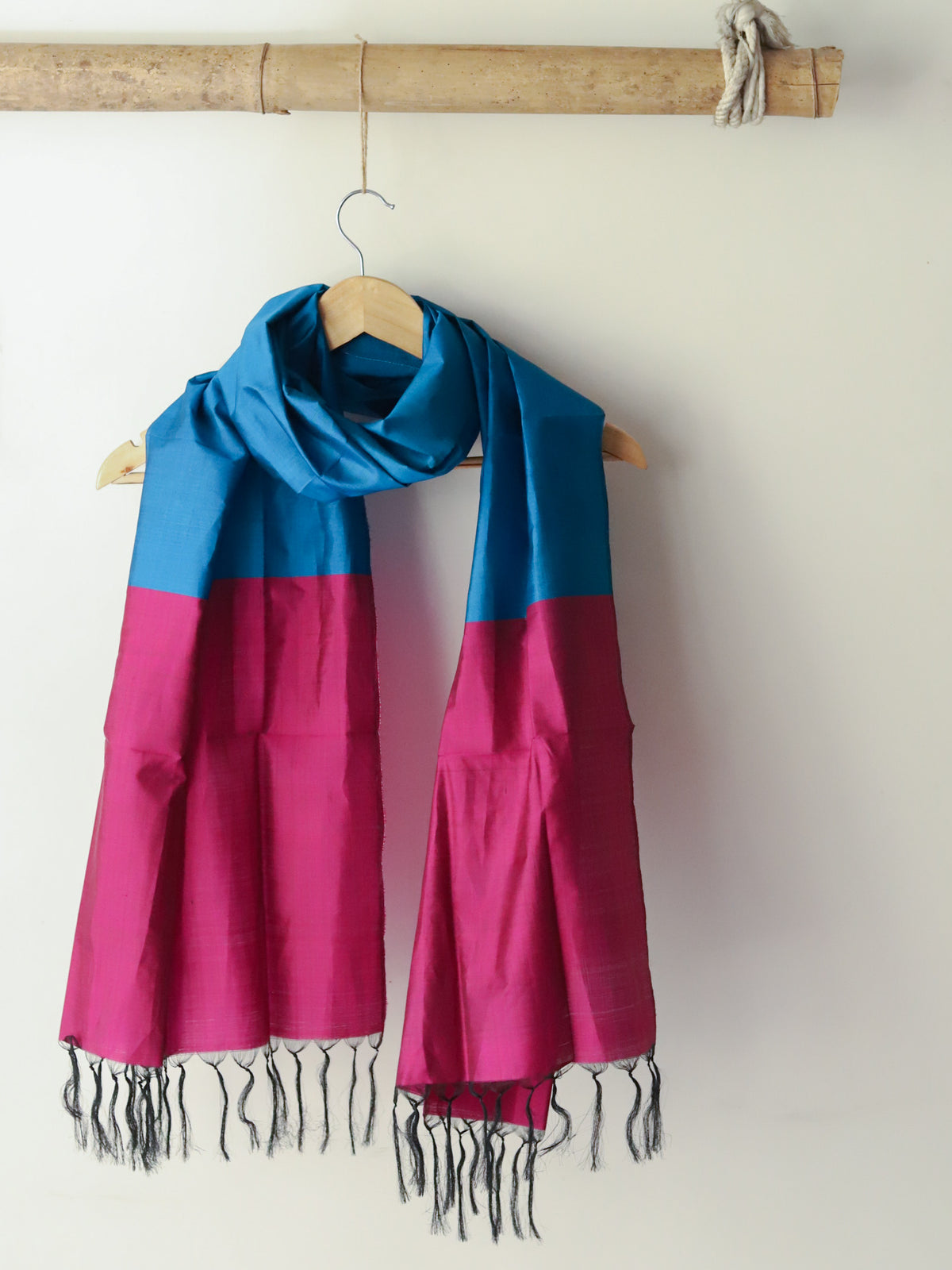 Two scarves, one blue and one pink, hanging on a wooden hanger against a white wall.
