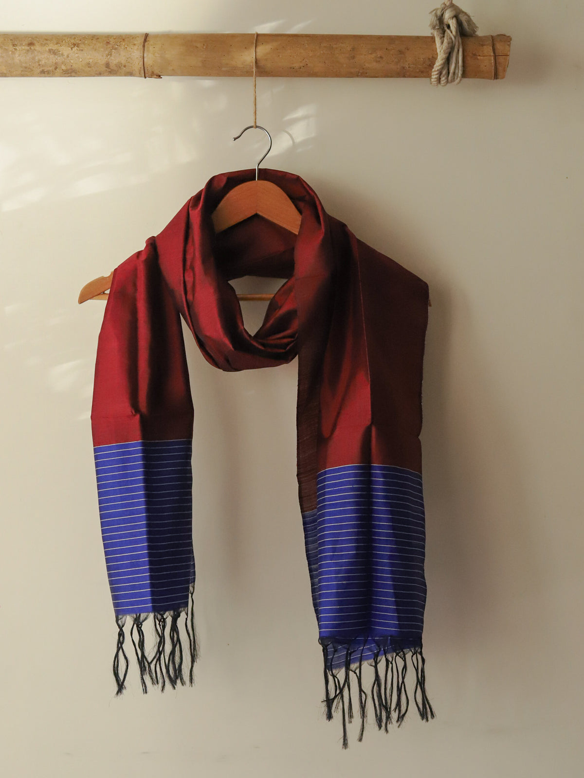 Red and blue striped scarf with tassels hanging on a wooden hanger against a beige wall.
