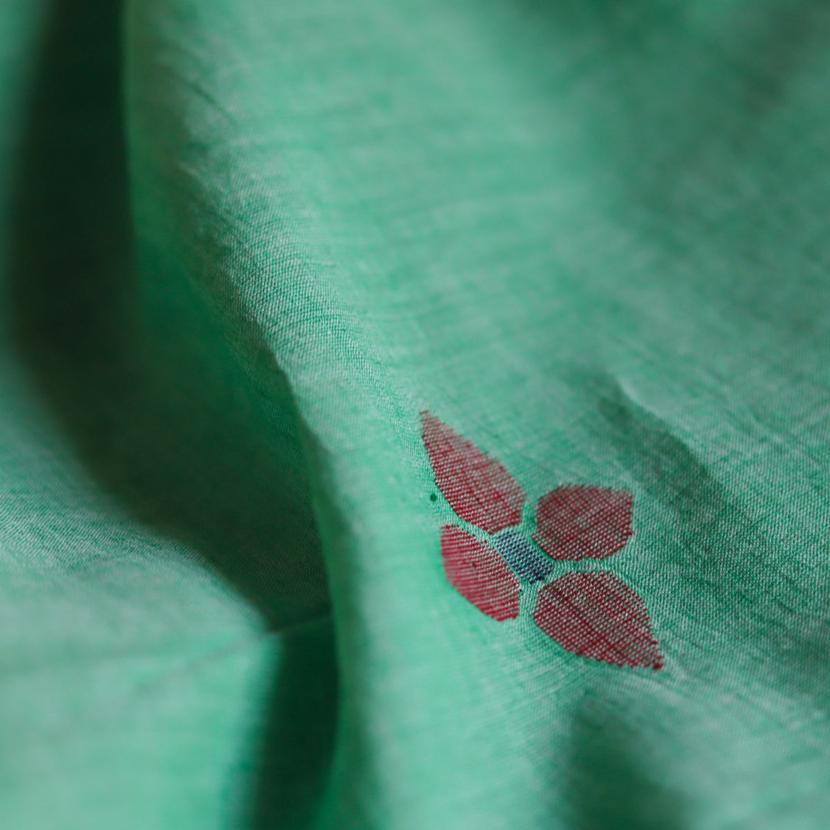 Close-up of green Bengal handwoven Jamdani fabric with a small red floral pattern