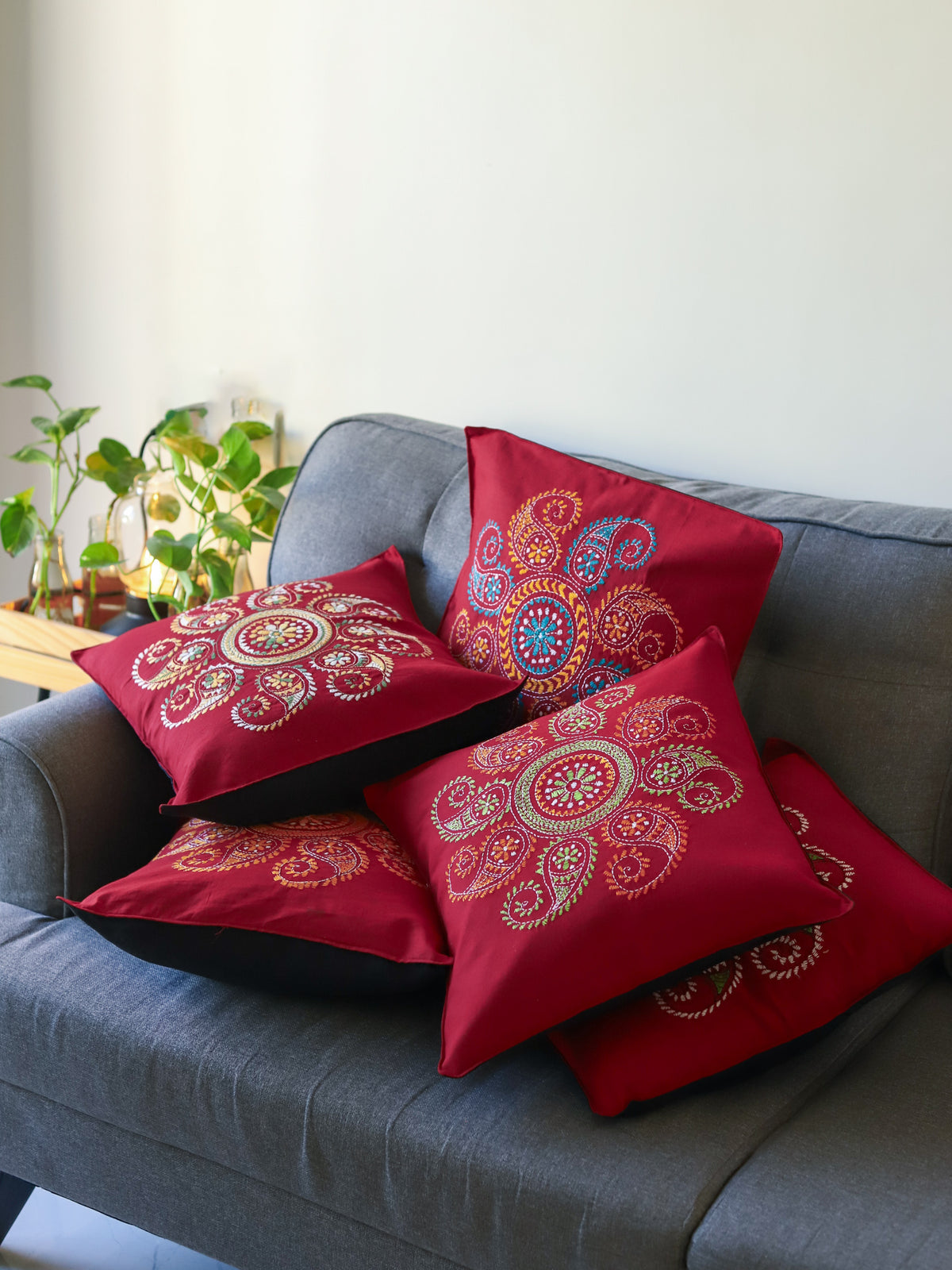 Bengal red patterned hand embroidery kantha cushions on a grey sofa with a neutral background next to green plants