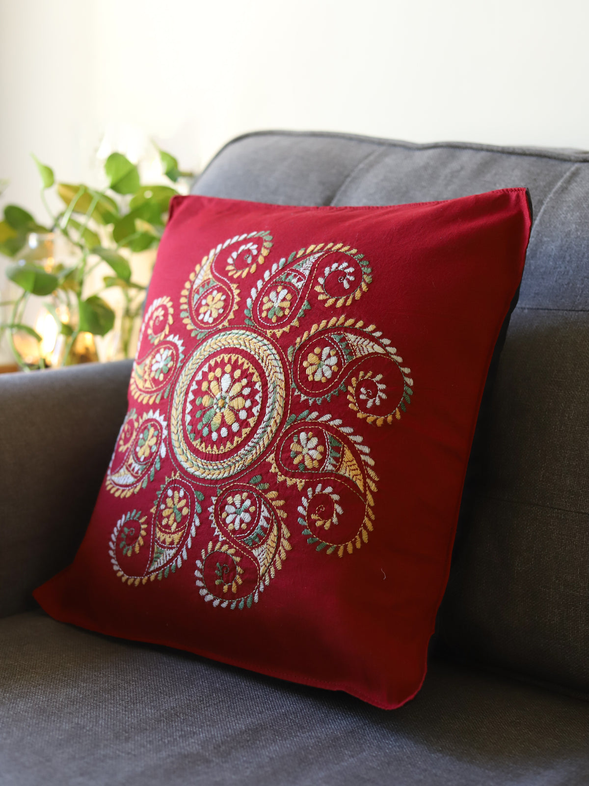 Red pillow with intricate gold embroidery on a gray couch