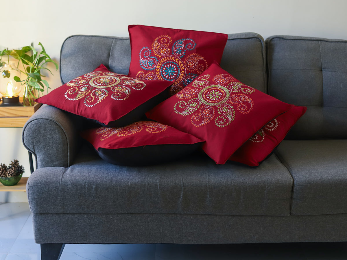 Bengal red patterned hand embroidery kantha cushions on a grey sofa with a neutral background next to green plants