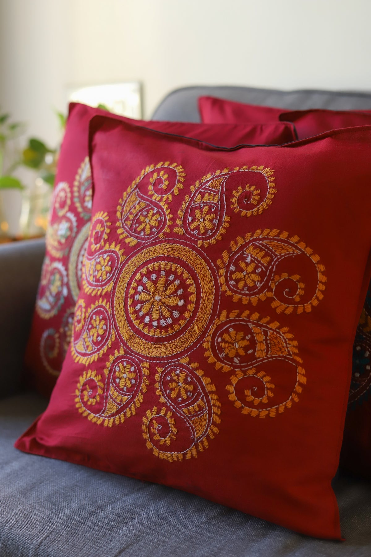 Red pillow with intricate gold embroidery on a gray couch.