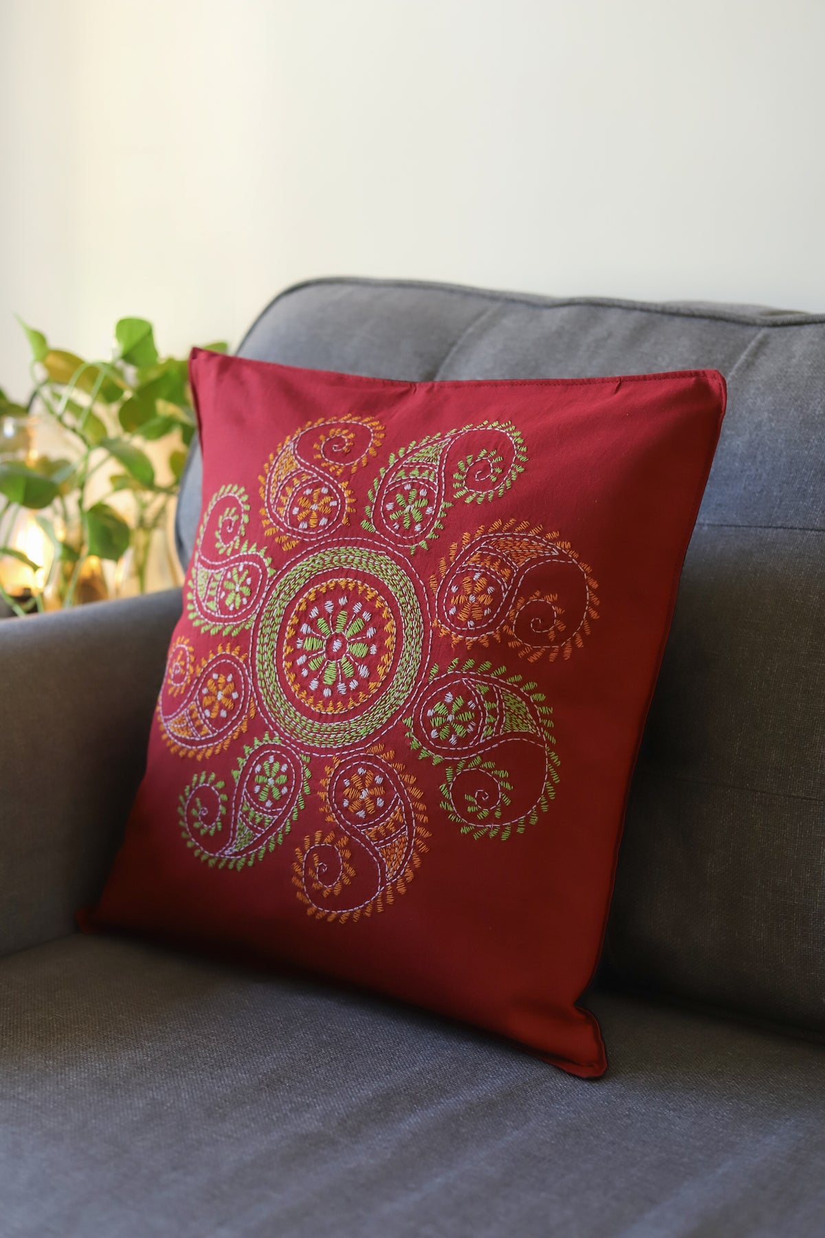 Red embroidered pillow on a gray couch with a blurred plant in the background