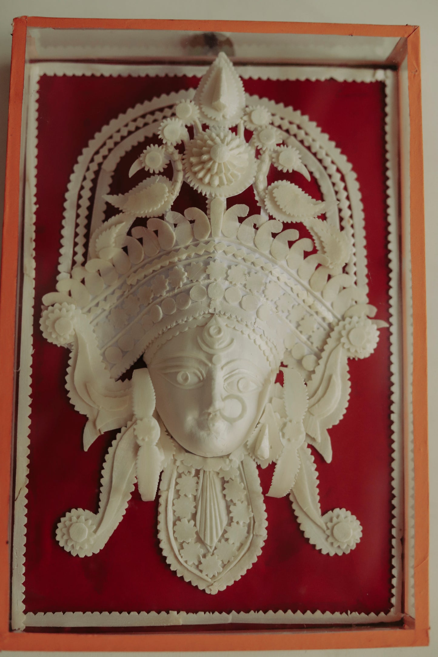 Decorative wall art of a Bengal sholapith face with intricate designs on a red background