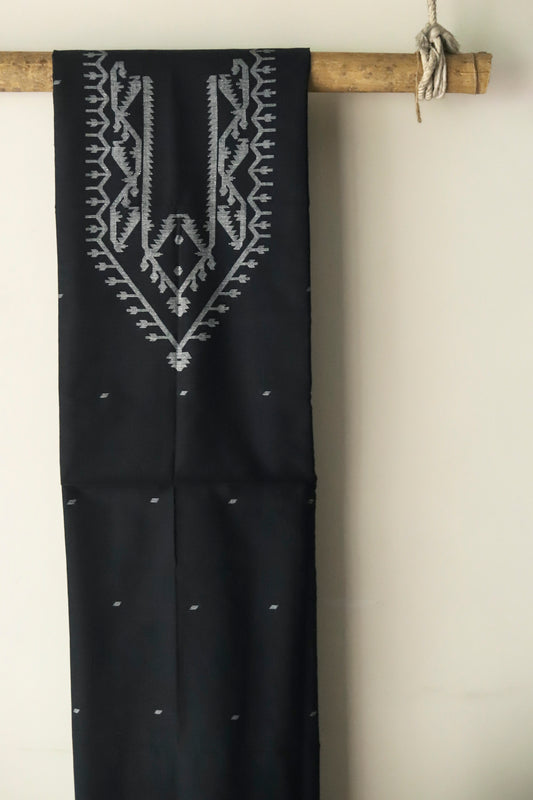 Black hand woven pure muslin cotton fabric of West Bengal with white patterns hanging on a wooden rod against a beige wall.