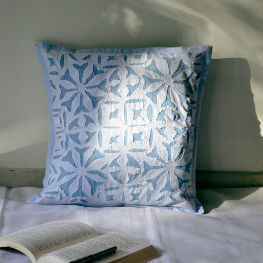 Handcrafted cushion cover with an orange and beige geometric pattern, placed on a couch next to a potted plant and a book.
