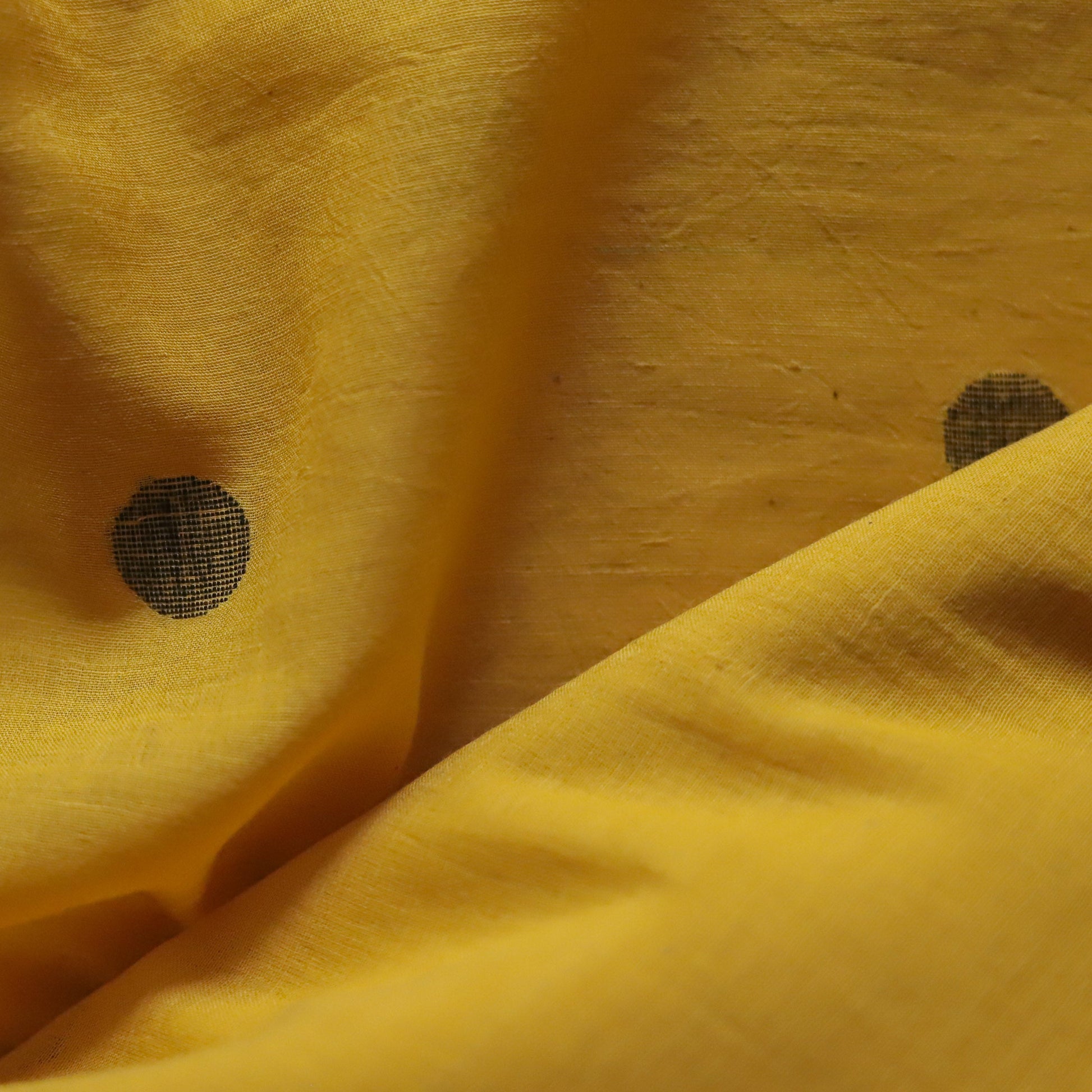 Close-up of handwoven yellow pure cotton fabric with black polka dots