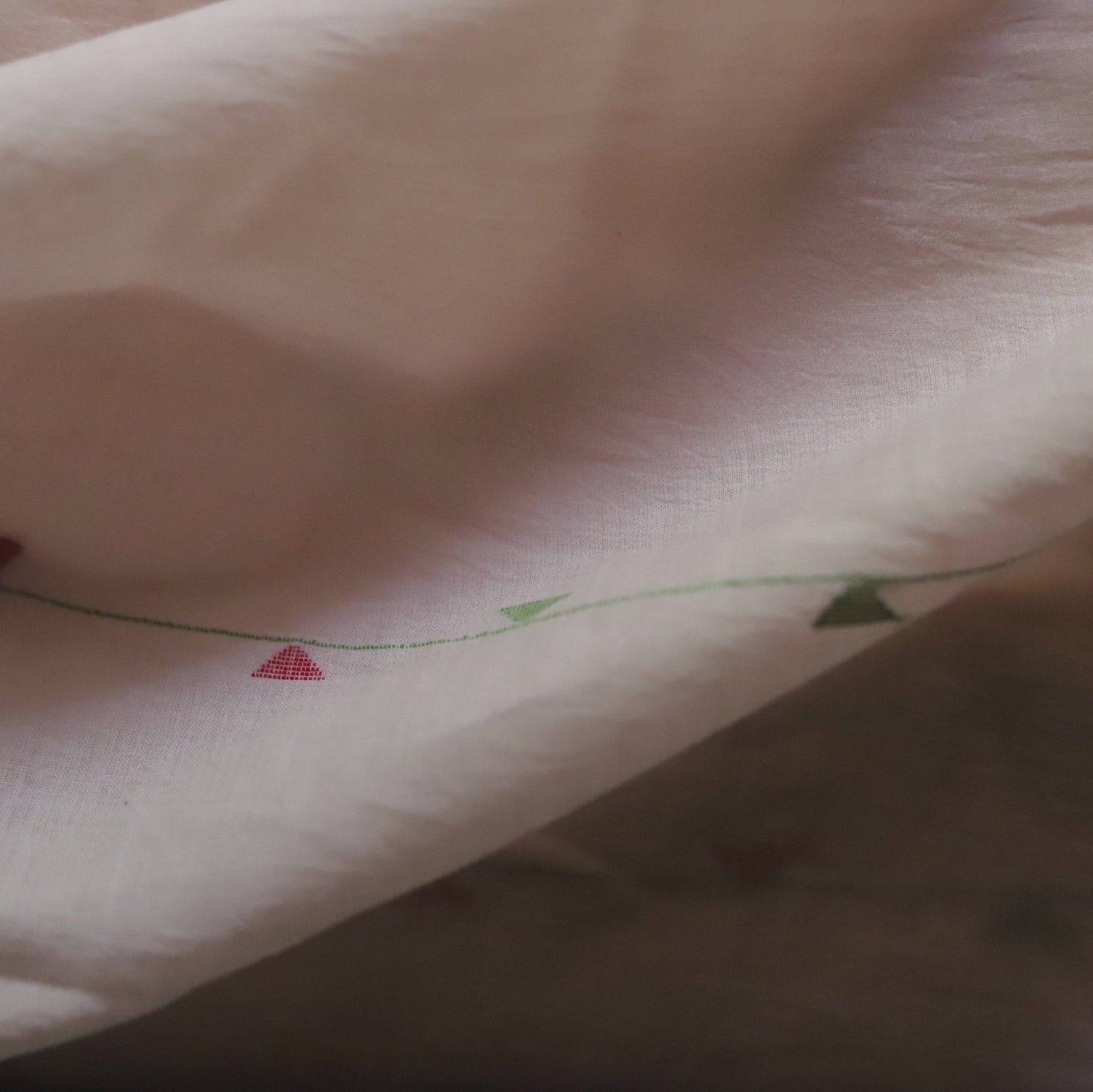 Close-up of a pink fabric with red heart patterns and green leaves.