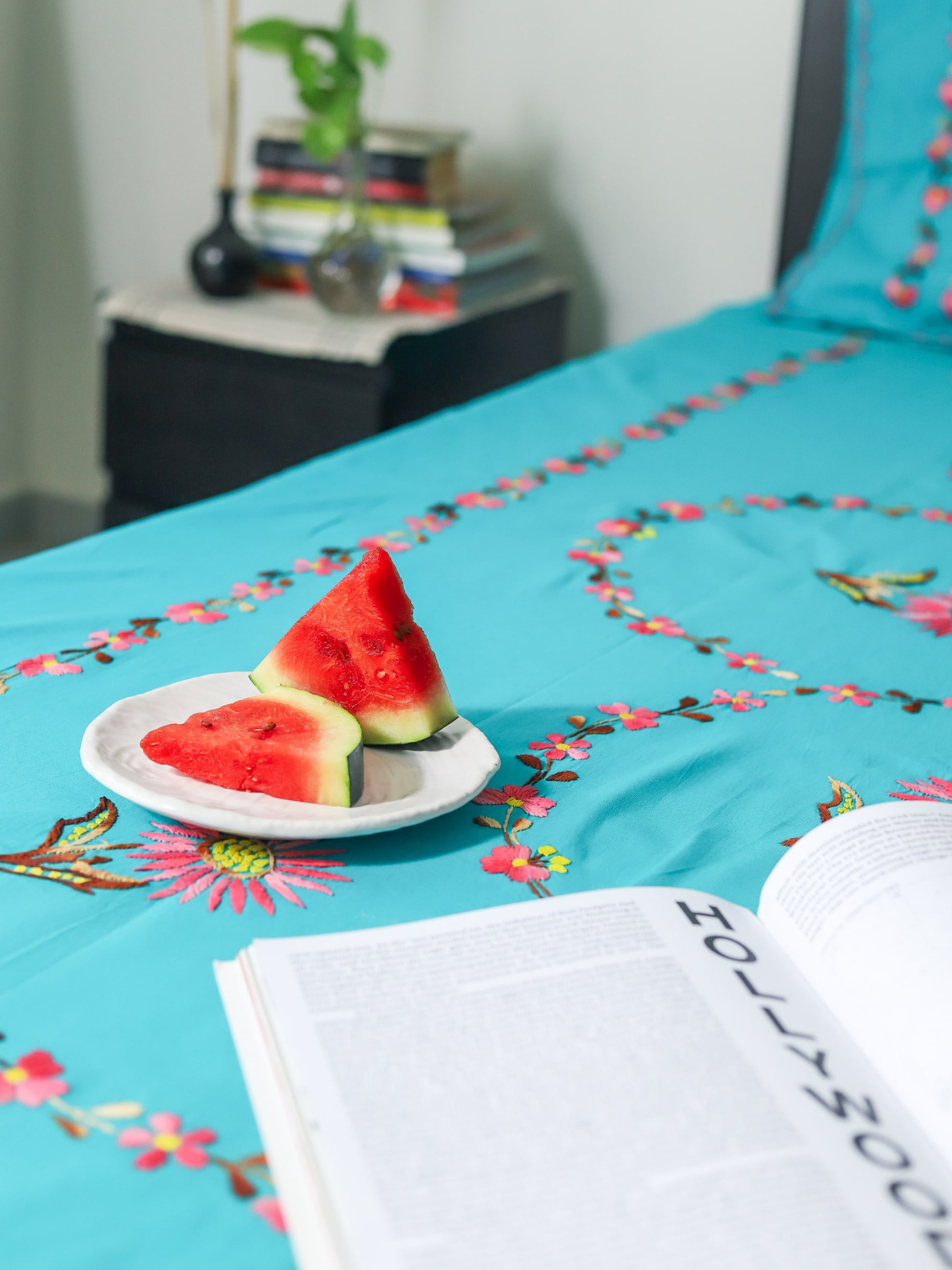 Turquoise bedspread with floral patterns and watermelon slices on a plate.