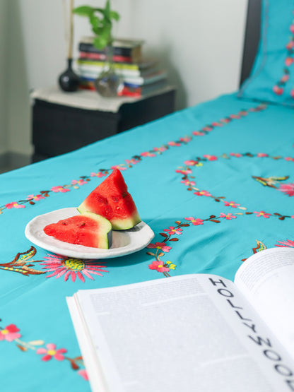 Turquoise bedspread with floral patterns and watermelon slices on a plate.