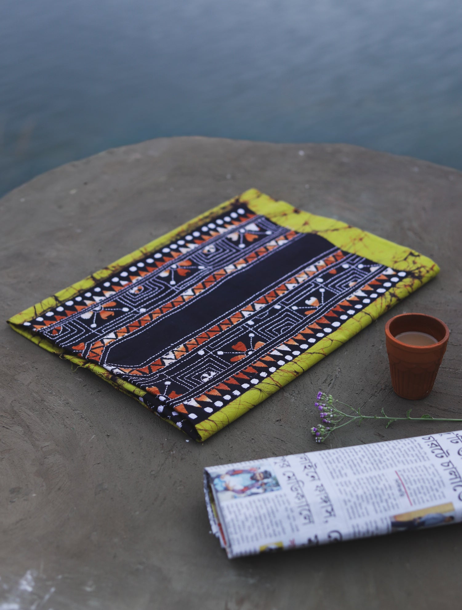 Decorative Batik Kantha Cotton Kurta Fabric with geometric pattern on a stone surface next to a cup of coffee and rolled-up newspaper.