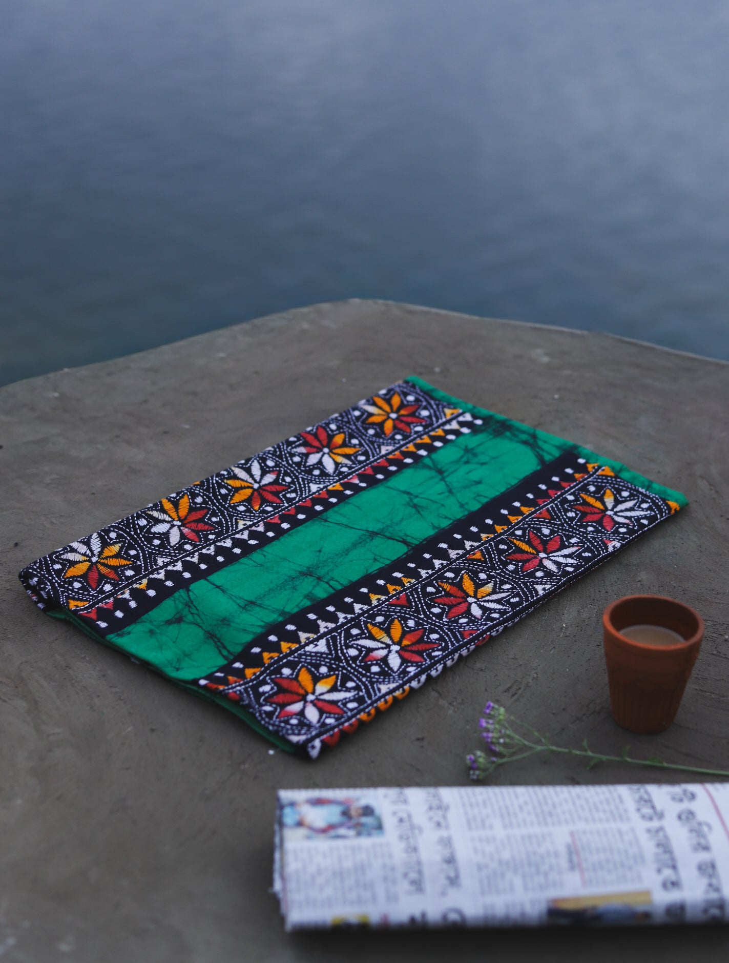 Decorative Batik Kantha Cotton Kurta Fabric with geometric pattern on a stone surface next to a cup of coffee and rolled-up newspaper.