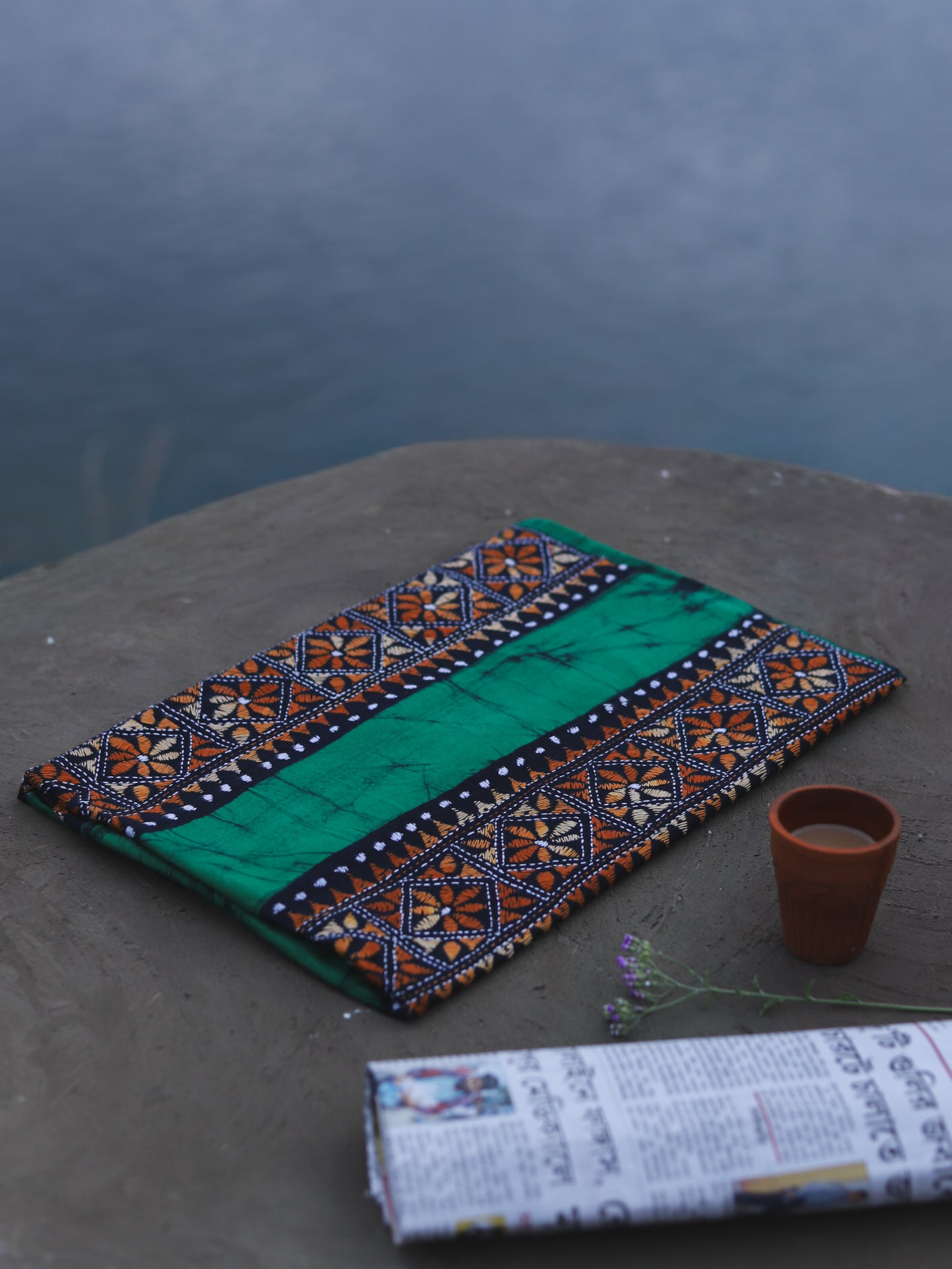 Decorative Batik Kantha Cotton Kurta Fabric with geometric pattern on a stone surface next to a cup of coffee and rolled-up newspaper.