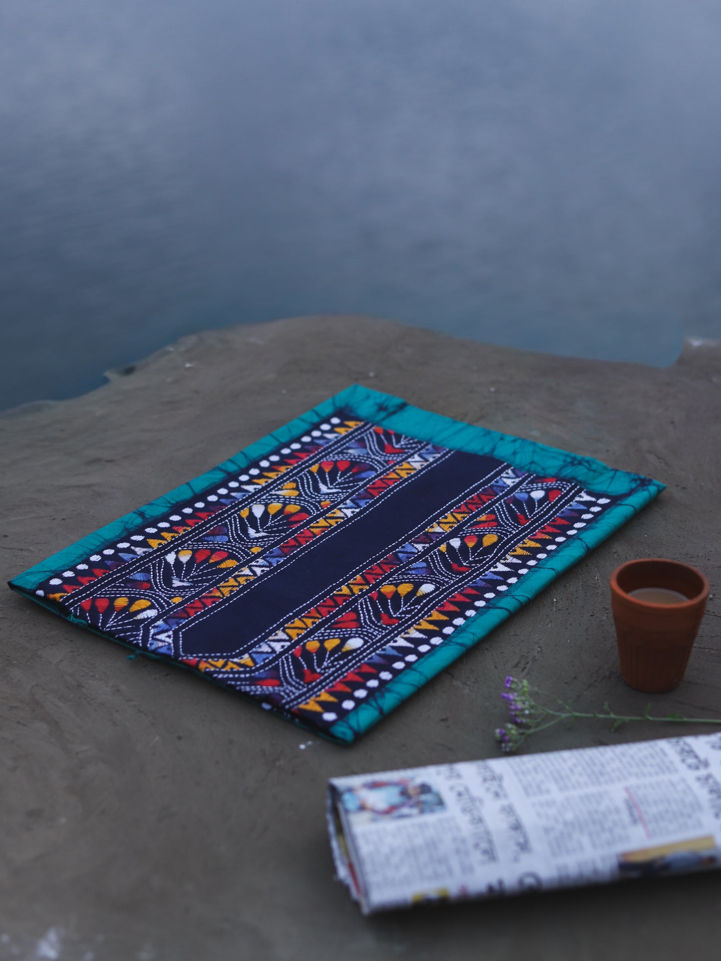 Decorative Batik Kantha Cotton Kurta Fabric with geometric pattern on a stone surface next to a cup of coffee and rolled-up newspaper.