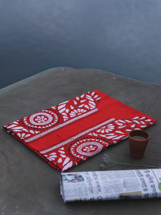 Red and white patterned fabric on a dark surface with a small cup and rolled-up newspaper.