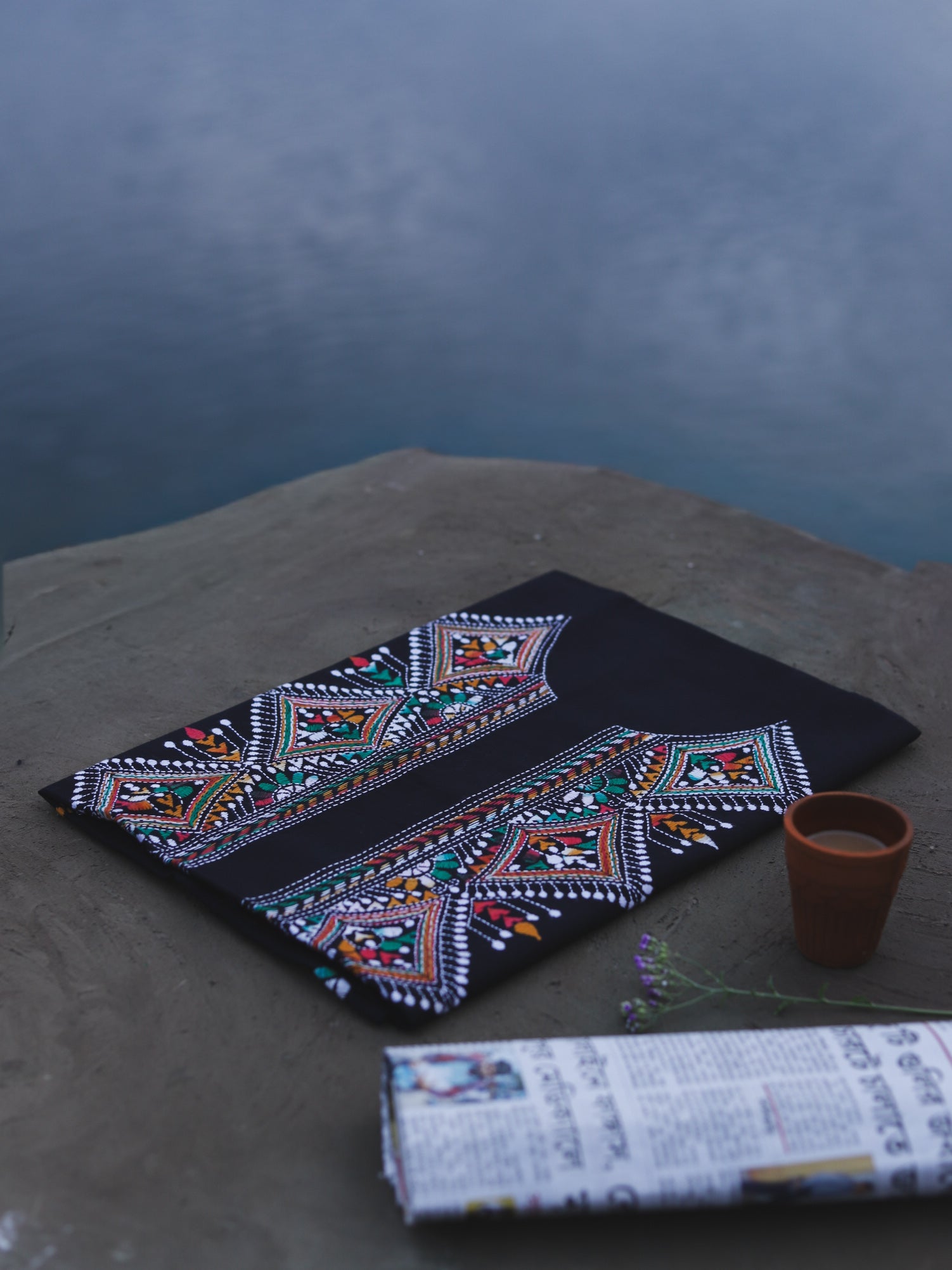 Embroidered fabric with geometric patterns on a dark surface, next to a small pot.