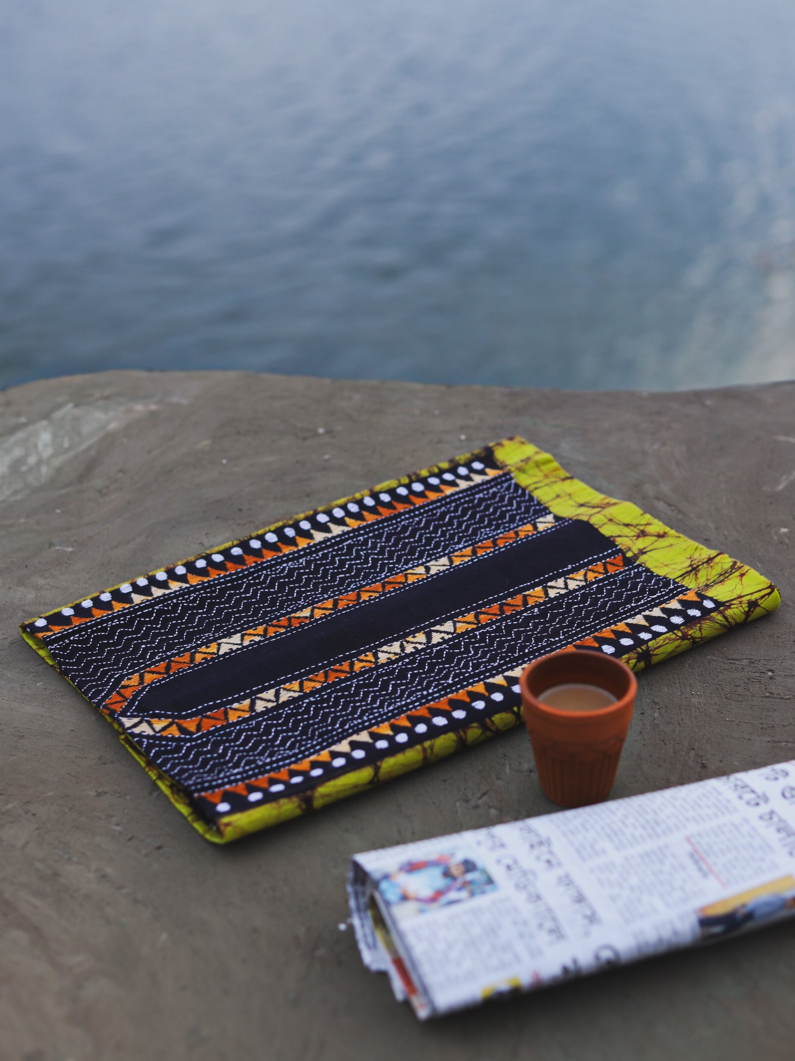 Decorative Batik Kantha Cotton Kurta Fabric with geometric pattern on a stone surface next to a cup of coffee and rolled-up newspaper.