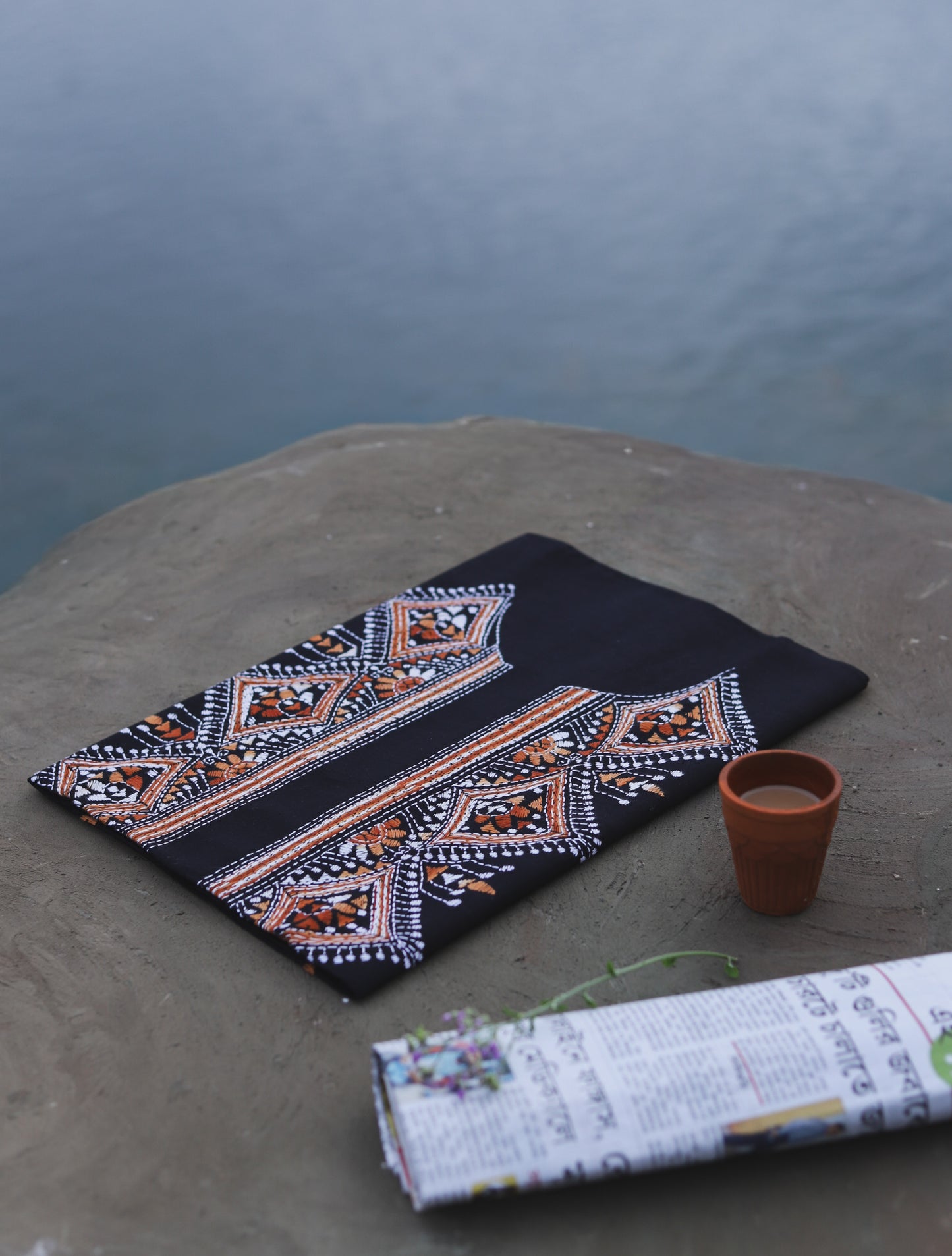 Embroidered cotton fabric with geometric patterns on a stone surface near a body of water.