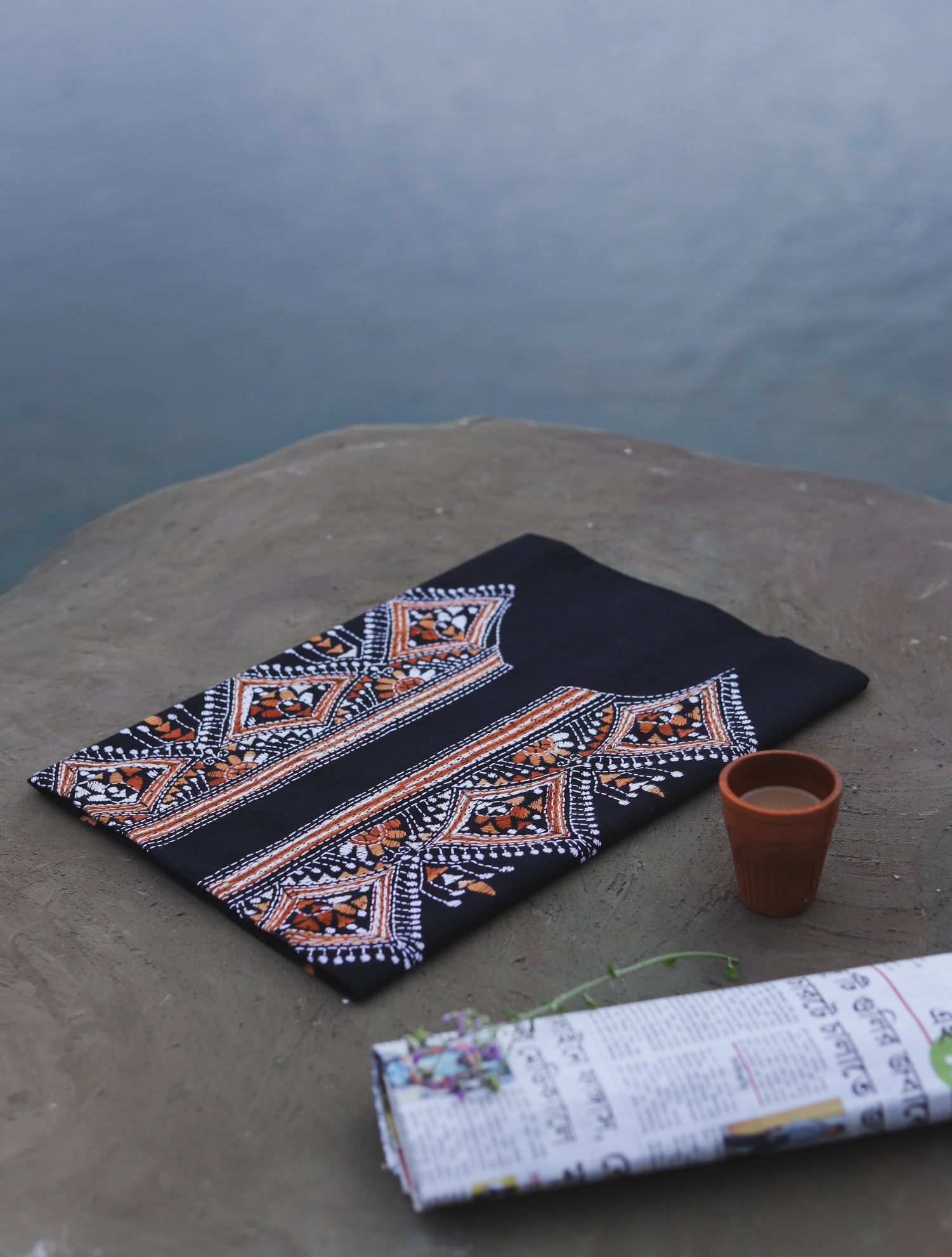 Embroidered cotton fabric with geometric patterns on a stone surface near a body of water.