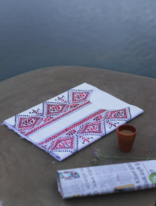 Embroidered cloth with bengali white red patterns on a wooden surface near a body of water