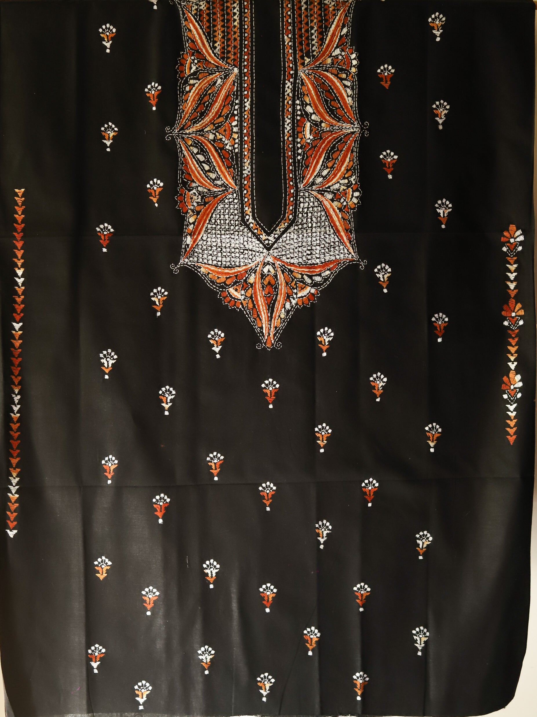 Black fabric with intricate orange and white embroidery on a dark background