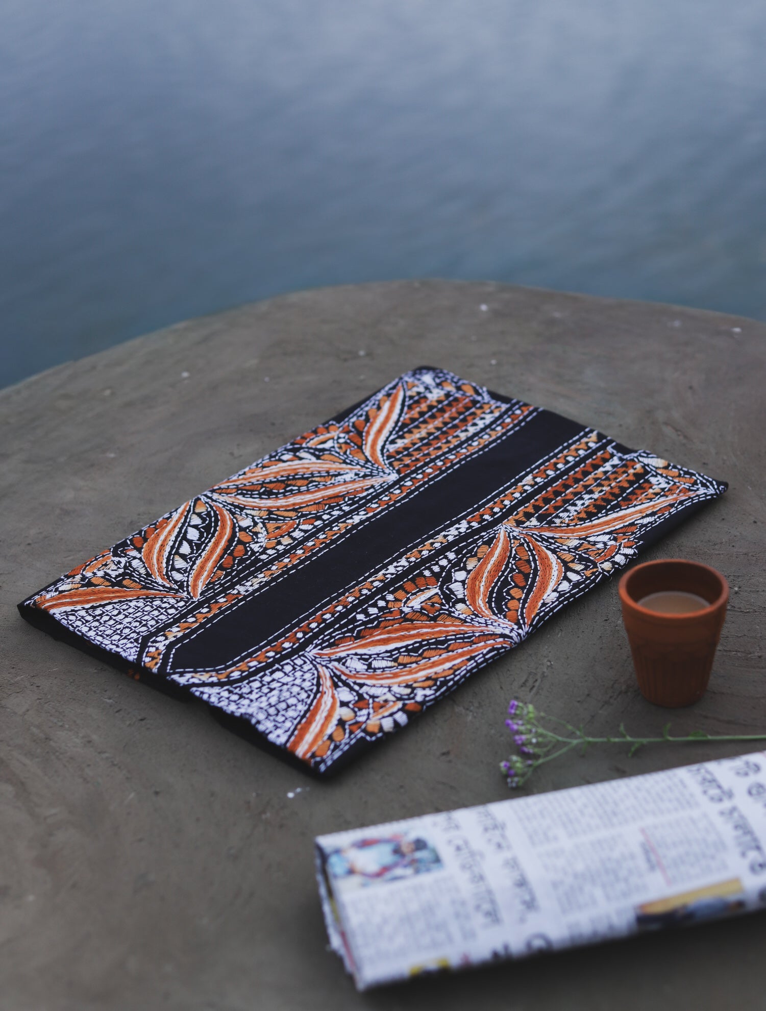 Embroidered cotton fabric with geometric patterns on a stone surface near a body of water.