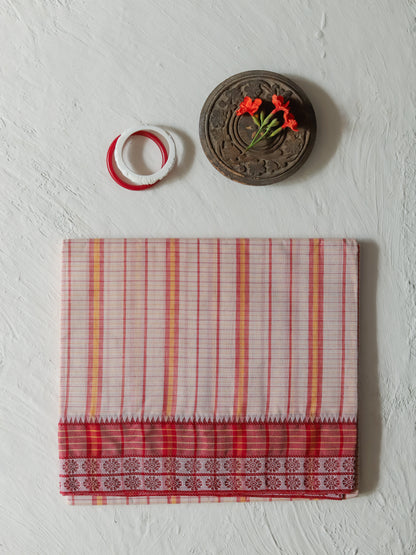 A folded Bengali red and white striped cotton sarong with a traditional ikat border, displayed on a textured white wall alongside decorative props