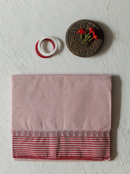 A folded Bengali white red cotton sari, featuring a red and white striped border with a paisley pattern, displayed on a textured off-white background with decorative props.