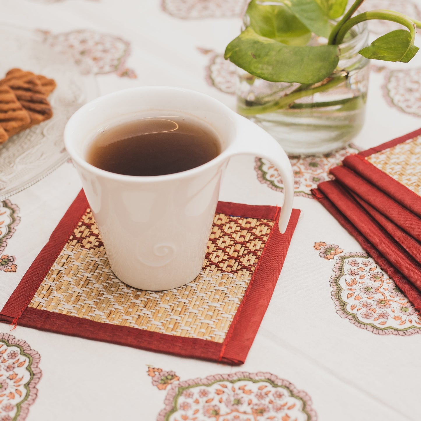 White mug with dark liquid on a patterned handwoven grass coasters with red borders