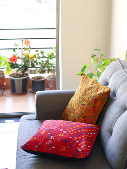 Gray sofa with colorful hand emberoidered Bengal kantha pillows in a room with plants and a sliding glass door.