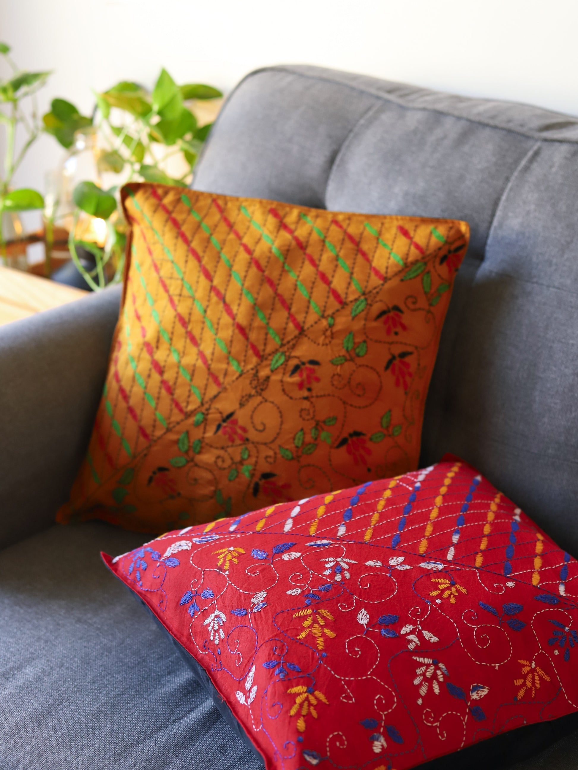 Decorative hand emberoidered Bengal kantha pillows with intricate patterns on a gray sofa.