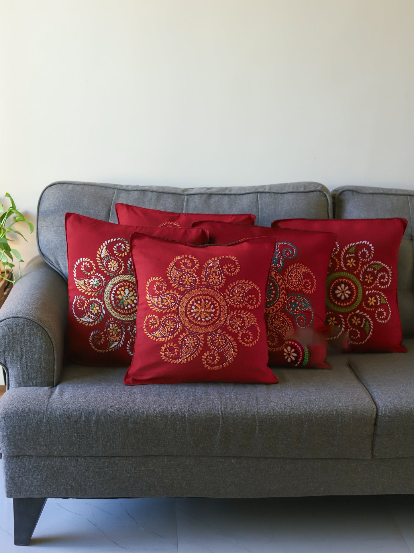Bengal red patterned hand embroidery kantha cushions on a grey sofa with a neutral background next to green plants