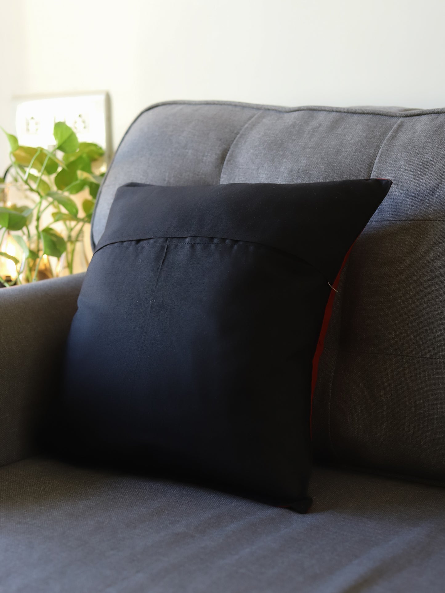 Black pillow on a gray couch with a plant in the background
