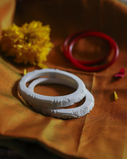 White ceramic ring with intricate design on a wooden surface with yellow flowers and a red object.