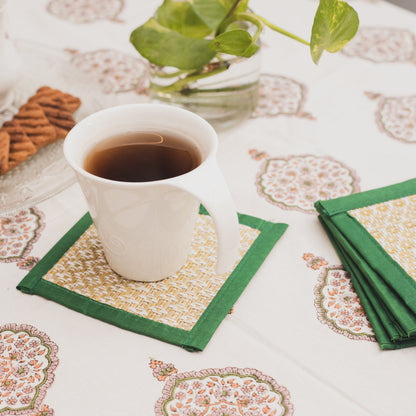 White cup of tea on a patterned tablecloth with green handwoven table coasters and cookies