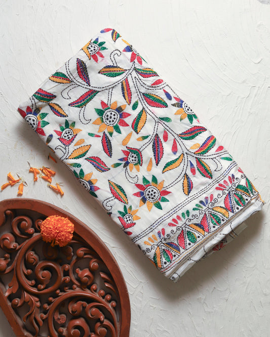 Decorative saree with colorful floral patterns on a white surface with a decorative pot.
